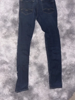 Mörkblå skinny jeans från Replay - Snygga mörkblå skinny jeans från Replay med klassiska bakfickor och diskreta sömmar. Jeansen har en smal passform och är tillverkade i ett stretchigt denimtyg som sitter tajt längs benen. Perfekta för en trendig och avslappnad stil.