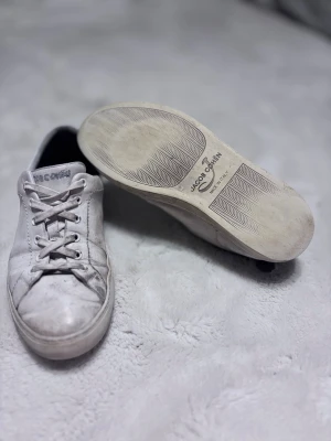 Vita sneakers från Jacob Cohen - Stilrena vita sneakers från Jacob Cohen med klassisk låg profil och snörning framtill. Skorna har diskreta logotyper på sidan och hälen samt en slitstark gummisula. Perfekta för en clean och avslappnad look.