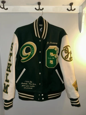 J.Lindeberg Baseball Jacka  - Snygg varsity baseball jacka från J. Lindeberg i grönt och vitt med broderade detaljer, stora siffror och bokstäver på ärmar och bröst. Jackan har ribbade muddar, tryckknappar och kontrastfärgade ärmar. Perfekt för dig som gillar streetwear och sportig stil. Nypris så kostar den 10 000kr. Den är sparsamt använd men kan ändå tänka mig att sälja för 6000kr men man kan alltid skicka prisförslag så får man se👍