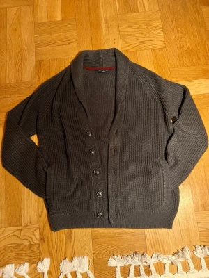 Mörkgrå kofta från Tokyo Laundry - Snygg mörkgrå kofta från Tokyo Laundry med grovstickad struktur och bred sjalkrage. Koftan har knäppning med sex knappar framtill och ribbade muddar vid ärmslut och nederkant. Perfekt för lager på lager och chill stil.