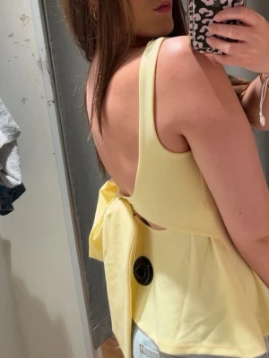 Gul topp med stor rosett från bikbok  - Supersöt ljusgul linnetopp med breda axelband och stor rosett i ryggen. Knappt använd och bra skick, skriv gärna vid fler frågor. Xs men passar som s