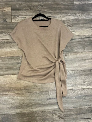 Beige topp med knyt från Zara - Stilren beige topp från Zara med rund halsringning och korta ärmar. Toppen har en snygg knytdetalj i sidan som ger en modern touch. Perfekt att matcha med både jeans och kjol för en trendig look. Aldrig använd🥰