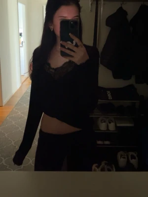 Svart topp med spetsdetalj - Snygg svart croppad topp med långa ärmar och v-ringning med spetskant. Perfekt för dig som gillar en trendig och feminin stil. Toppen har en tight passform och är riktigt bekväm.