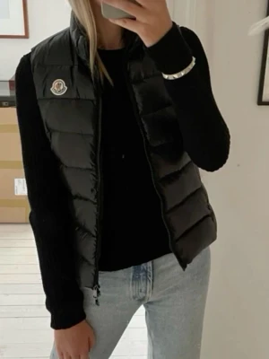 Svart dunväst med dragkedja - Snygg svart dunväst från Moncler med dragkedja och logotyp på bröstet. Västen har två praktiska fickor med dragkedjor framtill. !Inte äkta!