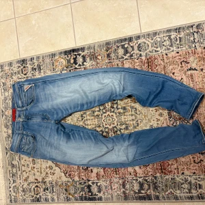 Ljusblå raka jeans från Replay - Säljer ett par ljusblå jeans från Replay med klassisk femficksdesign och raka ben. Jeansen har en snygg tvättad look och röda detaljer vid fickan. Perfekta för en avslappnad stil och tillverkade i hyperstretch denimtyg. Inga defekter och priset är inte hugget i sten!