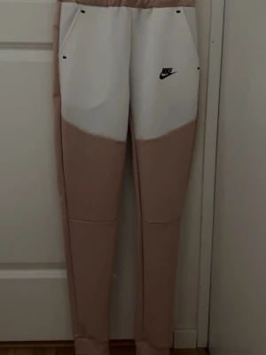 Nike beige och vit hoodie med dragkedja - Säljer en snygg hoodie från Nike i beige och vitt med svart logga på bröstet. Hoodien har dragkedja framtill, två fickor, huva med vita snören och en svart detaljficka på ena ärmen. Materialet känns mjukt och sportigt, perfekt för en avslappnad streetwear-look.