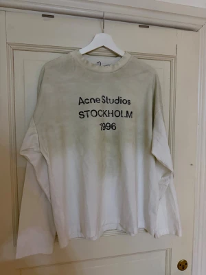 Beige långärmad t-shirt Acne Studios - Säljer en beige långärmad t-shirt från Acne Studios med trycket 'STOCKHOLM 1996' på bröstet. Oversized passform och rund halsringning. Perfekt för dig som gillar minimalistisk och stilren design.