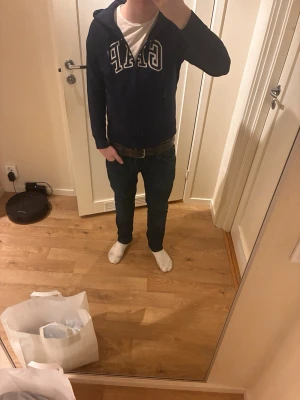 Mörkblå hoodie från GAP med dragkedja - Snygg mörkblå hoodie från GAP med vit logga framtill och dragkedja. Tillverkad i 60% bomull. Klassisk huva och kängurufickor gör den både stilren och bekväm. Storlek s men känns som xs