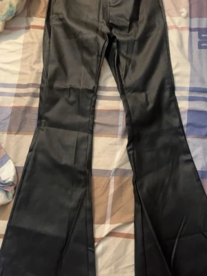 Svarta bootcut jeans i glansigt material - Snygga svarta skin jeans med bootcut-modell och glansig finish. Byxorna har en klassisk femficksdesign och markerad söm längs benen. Perfekta för dig som vill sticka ut med en trendig look.