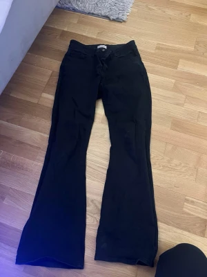 Svarta bootcut jeans från Lindex - Snygga svarta bootcut jeans från Lindex med klassisk femficksdesign och normal midja. Jeansen har utsvängda ben och är tillverkade i ett mjukt bomullsmaterial med lite stretch för extra komfort. Perfekta för en trendig och avslappnad look.