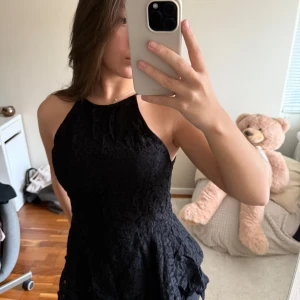 Svart spetsblus med peplum - Säljer en svart blus med spets och peplumskärning. Toppen har hög halsringning och är ärmlös, vilket ger en stilren och trendig look. Perfekt att styla med jeans eller kjol för en snygg outfit.