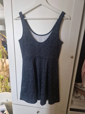 Mörkblå prickig klänning Divided - Söt mörkblå kortklänning från Divided by H&M med vitt prickigt mönster. Klänningen är ärmlös med rundad urringning och har en lätt utställd kjol. Perfekt för dig som gillar enkel men stilren design.