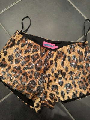 Leopardmönstrade paljettshorts Eclipse - Säljer ett par riktigt statement leopardmönstrade shorts från Edikted, täckta med glittriga paljetter. De har en tight passform och elastisk midja. Perfekta för dig som vill sticka ut och älskar djurmönster och glitter.