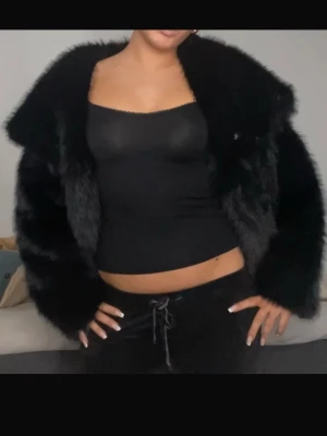 Svart fluffig pälsjacka - Säljer en svart, kort pälsjacka med bred krage och oversized passform. Jackan har en lyxig, mjuk känsla och stängs framtill med diskreta knappar. Perfekt för dig som vill ha en statement piece i garderoben.