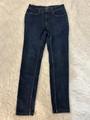 Mörkblå skinny jeans från Vero Moda - Säljer ett par mörkblå skinny jeans från Vero Moda i Strl: S/L30, med klassisk femficksdesign och kontrastsömmar. Jeansen har normal midja, bälteshällor och är tillverkade i stretchigt denimtyg för en bekväm passform.