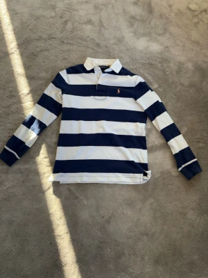 Ralph lauren tröja  - En riktigt snygg långärmad piké från varumärket polo talph lauren. Tröjan har storleken small och är i riktigt bra skick. Det är en riktigt snygg tröja med blå och vita tjocka ränder. Passar bra till många andra kläder.
