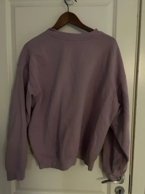 Ljuslila sweatshirt från H&M Divided - Sweatshirt i ljuslila från H&M Divided, storlek S. Klassisk rund hals och långa ärmar med ribbade muddar. Mjuk bomullskvalitet som är skön att ha på sig. Perfekt för chill dagar och enkel att matcha med jeans eller mjukisbyxor. Säljer då den ej används längre