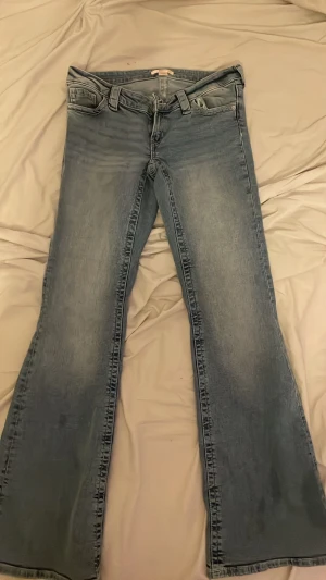 Bootcut jeans i ljusblå denim - Säljer ett par ljusblå bootcut jeans med klassisk femficksdesign och utsvängda ben. Jeansen har snygga slitningar och broderade detaljer på bakfickorna. Perfekta för en avslappnad och trendig look.