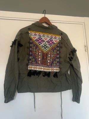 Olivgrön jeansjacka med broderi - Snygg olivgrön jeansjacka från Bershka med färgglatt broderi och tofsar på ryggen. 