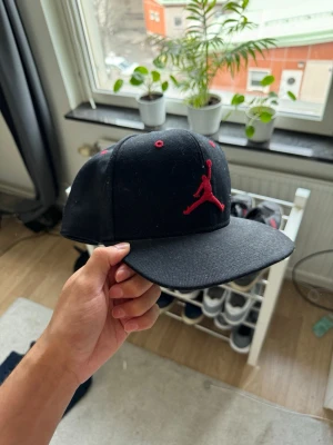 Svart Jordan keps med röd logga - Snygg svart keps från Jordan med den klassiska Jumpman-loggan broderad i rött framtill. One size