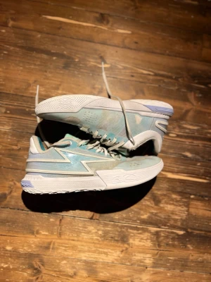 Blåvita sneakers från Li-Ning - Snygga sneakers från Li-Ning i ljusblått och vitt med grå detaljer. Skorna har en låg siluett, mesh- och syntetmaterial för bra andningsförmåga och en chunky vit sula med mönstrad undersida. Perfekta för dig som gillar sportig och modern stil.