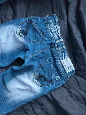 Blå bootcut jeans från Crazy Age - Säljer ett par blå bootcut jeans från Crazy Age med broderade detaljer på bakfickorna. Jeansen har låg midja, tillverkade i denim med stretch. Perfekta för dig som gillar retrostil och vill ha ett par unika jeans. Skriv om du har några frågor gällande pris eller mått💕