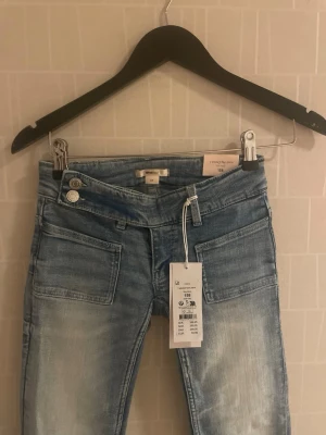 Blå bootcut low waist jeans  - Snygga ljusblå bootcut jeans från Gina  med slitningar och broderad bakficka med paljettdetaljer. Jeansen har två framfickor, dubbla knappar i midjan och är tillverkade i bomullsdenim med lite stretch för skön passform.