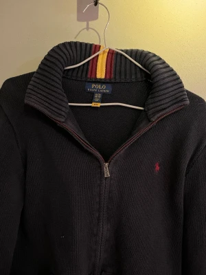 Polo Ralph Lauren zip-up - Säljer en zip-up tröja från Ralph Lauren. Den är i rätt bra skick, lite sliten men inget större problem. Den är stickad med en röd broderad logga på bröstet. Den är i storlek XL i barn storlek men passar som S i vuxen storlek.