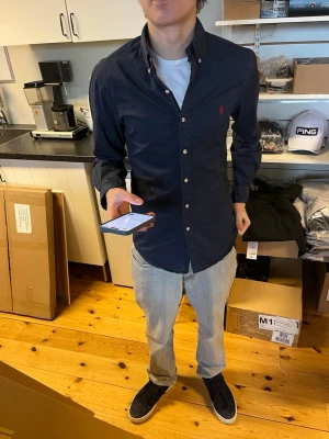 Mörkblå skjorta från Ralph Lauren - Snygg mörkblå skjorta från Ralph Lauren i slim fit-modell. Skjortan har klassisk krage, knappar framtill och den ikoniska röda loggan broderad på bröstet. Tillverkad i lätt bomullstwill som känns skön mot huden.