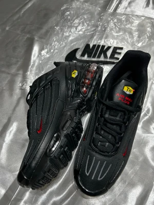 Nike Air Max Plus svarta sneakers - Nike Air Max Plus sneakers i svart med röda detaljer och Tn Air-logga. Ovandel i mesh och syntet, robust sula med Tuned Air-teknologi. Snygga reflekterande linjer på tån och klassisk snörning. Perfekta för dig som vill sticka ut med en sportig vibe.