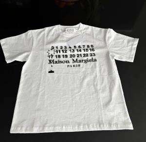 Vit Maison Margiela t-shirt med blurred tryck - Vit t-shirt från Maison Margiela med svart och grått pixelinspirerat tryck framtill och klassisk rund hals. T-shirten har korta ärmar och är tillverkad i mjuk bomull. Helt ny säljer pga för stor