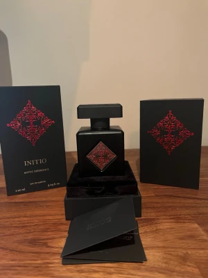 Initio Mystic Experience parfym 90ml - Lyxig parfym från Initio, Mystic Experience, i en matt svart fyrkantig flaska med röd dekorativ detalj och silverfärgad metallplatta på locket. Flaskan rymmer 90 ml och kommer i elegant svart förpackning med röda detaljer. Perfekt för dig som gillar exklusiva dofter.
