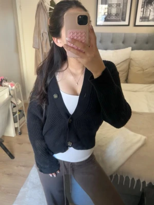 Svart ribbstickad kofta med knappar - Säljer en svart ribbstickad kofta med v-ringning och stora knappar framtill. Koftan har långa ärmar och breda muddar. ❤️❤️💖💞
