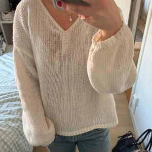 Vit stickad v-ringad tröja - Mysig beige stickad tröja med v-ringning och avslappnad passform. Tröjan har långa ärmar med breda muddar och är perfekt för lager-på-lager-stil. Enkel och stilren design som passar till jeans eller kjol.