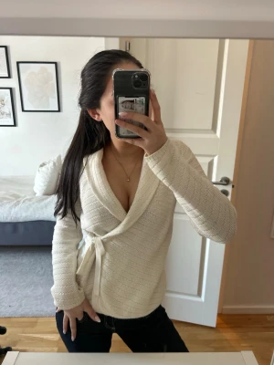 Krämvit omlottstickad tröja - Säljer en superfin krämvit stickad omlott-tröja med knytband i sidan. Tröjan har lång ärm och bred krage!!! ✨✨❤️💗🫶