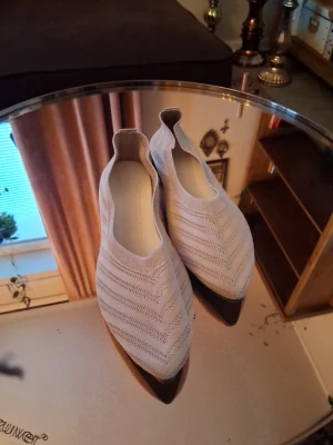 Beige stickade ballerinaskor - Snygga beige ballerinaskor med stickat mönster och spetsig tå. Skorna har låg sula och är tillverkade i ett mjukt textilmaterial som ger en modern och stilren look. Perfekta för dig som gillar minimalistisk och trendig design.