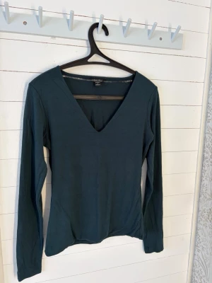 Mörkgrön/blå v-ringad långärmad tröja - En mörkgrön/blå v-ringad tröja från NewYorker. Den är i storlek M, men lite tajtare i passformen. Bara använd ett fåtal gånger. Hör av dig om du undrar något!