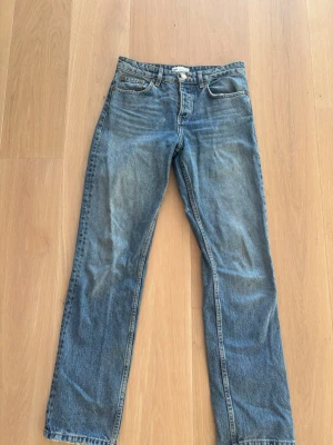 Blå raka jeans med fem fickor - Klassiska blå jeans med rak passform och fem fickor. Jeansen har en tidlös tvätt och normal midja, perfekta för en avslappnad stil. Tillverkade i slitstarkt denimtyg och har bälteshällor samt knappgylf. Strl 36, från Zara