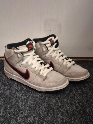 Nike SB DUNK High pro prm - Nike SB DUNK High pro prm. Beigea höga med svart nike logga och orangea detaljer. Begiea och svarta snören fås med. Varje sko har engen unik lapp på plösen. Höger sko har en unik sula där det ser ut som man har gått i ett tuggummi. Original box fås med.