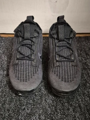 Nike Air Vapormax svarta - Säljer ett par svarta Nike Air Vapormax Flyknit sneakers med stickad ovandel och helt luftad sula. Dom är svarta med lite graffiti stänk på, mestadels på sulan. Väldigt bra skick. 