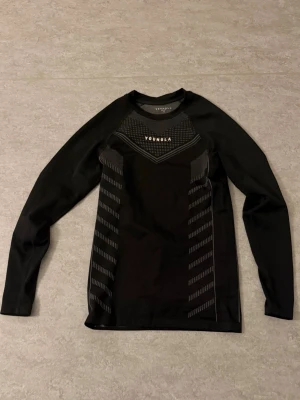  YoungLA compression  - Svart långärmad träningströja från YoungLA med diskreta gråa mönsterdetaljer på framsidan. Tight passform och rund halsringning, perfekt för gym eller löpning. Tillverkad i ett stretchigt funktionsmaterial som andas.