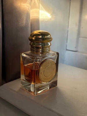 Burberry Goddess parfymflaska guld - Burberry Goddess parfym i en lyxig fyrkantig glasflaska med guldig metallkork och rund guldplakett framtill. Flaskan har en elegant och exklusiv design med bärnstensfärgad vätska inuti. Perfekt för dig som gillar stilrena och klassiska dofter.