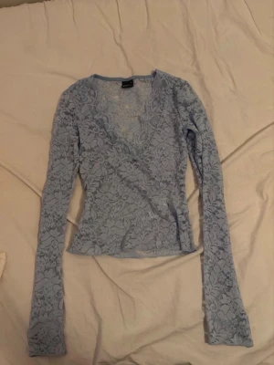 Ljusblå spets topp! - Supersöt ljusblå långärmad topp i spets med omlottdesign och v-ringning. Perfekt att styla med jeans eller kjol för en trendig look. Tunt och stretchigt material som sitter snyggt på kroppen.