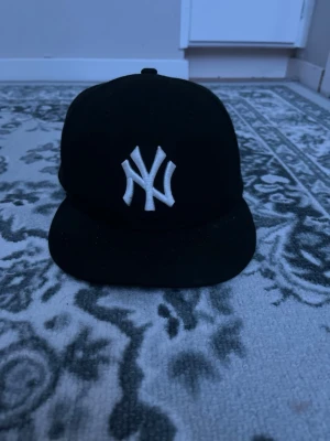 Svart New Era Yankees keps - Säljer en svart keps från New Era med klassiskt New York Yankees-broderi i vitt framtill. Kepsen har rak skärm och broderad New Era-logga på sidan. Perfekt för dig som gillar streetwear och sportig stil.