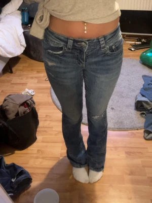 Blå bootcut jeans med slitningar - Säljer ett par blå bootcut jeans med slitningar på låren och knäna. Jeansen har klassisk femficksdesign och normal midja. Perfekta för en avslappnad och trendig look. Aldrig använda endast testade.