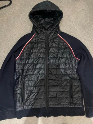 Tommy hilfiger cardigan jacka ”Pris kan diskuteras” - Snygg blå vindjacka med quiltad framsida och huva. Ärmar och rygg i mjukt tyg, ribbade muddar och dragkedja framtill. Röda och vita detaljer längs axlarna ger en sportig look. Två fickor med dragkedja på framsidan.