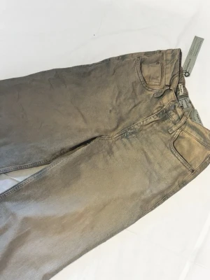 Beige jeans från Weekday - Snygga  jeans från river Island med klassisk femficksdesign och raka ben. Jeansen har bälteshällor och knappgylf. Tillverkade i bomull med en cool tvättad look. Perfekta för dig som gillar en avslappnad och trendig stil.