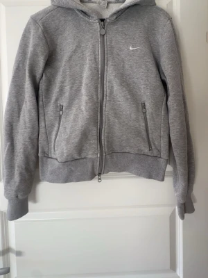 Grå zip hoodie från Nike - Snygg grå hoodie från Nike med dragkedja framtill och två fickor med dragkedja. Pris kan diskuteras! Storlek m men skulle säga att den även passar s!