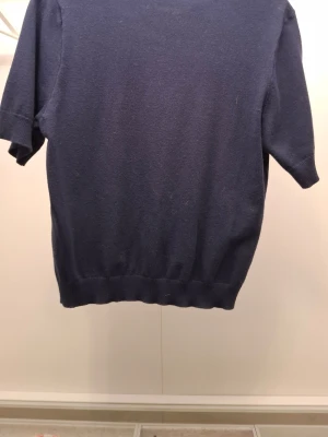 Mörkblå stickad polotopp med knappar - Mörkblå stickad polotopp från Selected Femme med korta ärmar och tre knappar framtill. Klassisk krage och ribbade muddar vid ärmslut och nederkant. Perfekt för en stilren och enkel look.