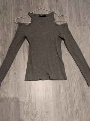 Grå ribbad topp med cut out från FB Sister - Trendig grå långärmad topp från FB Sister i ribbat material. Toppen har cut out-detaljer vid axlarna och en hög halsringning. Perfekt för dig som gillar en stilren men edgy look.